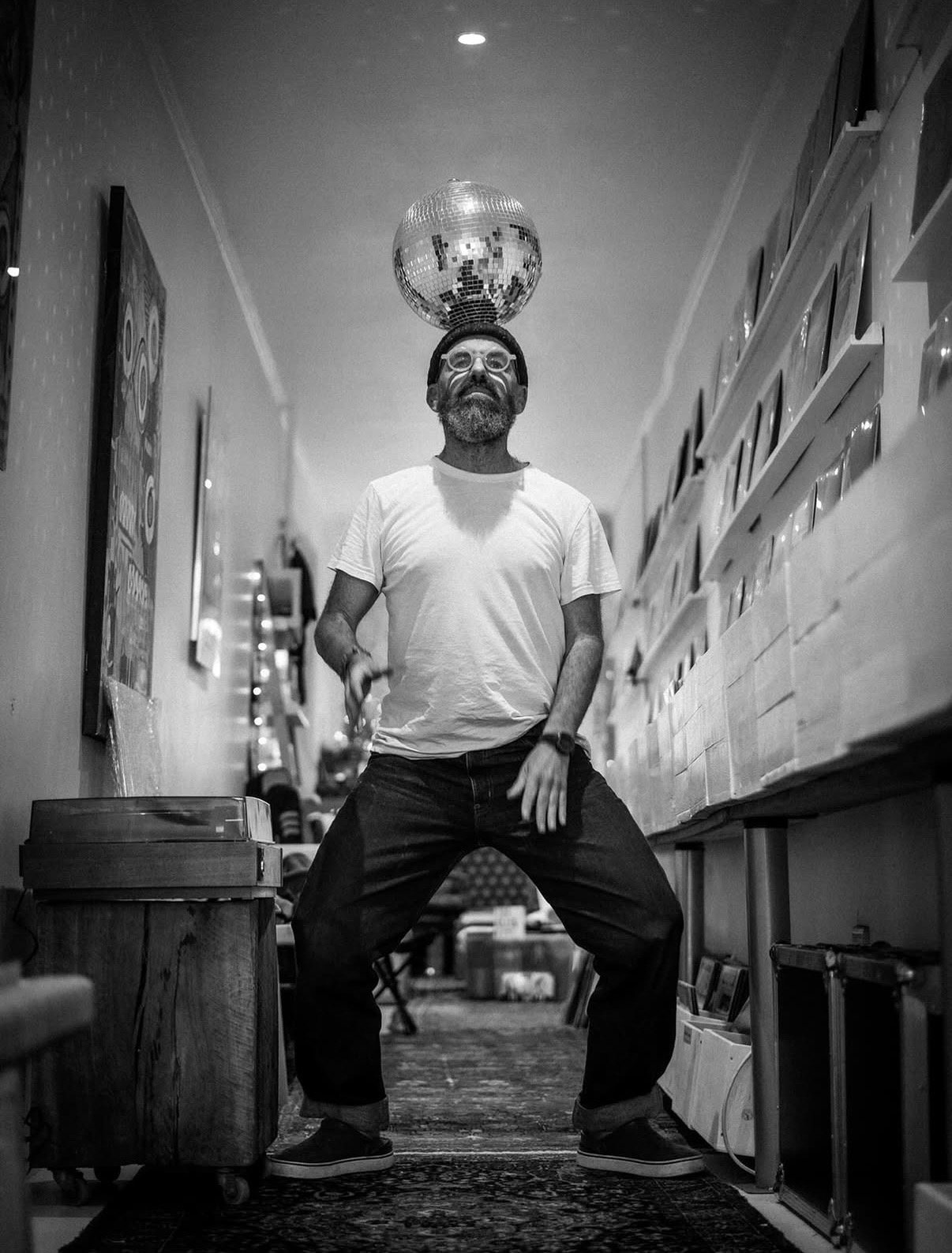 A man balancing a disco ball on his head between the record racks at Slow Life Records